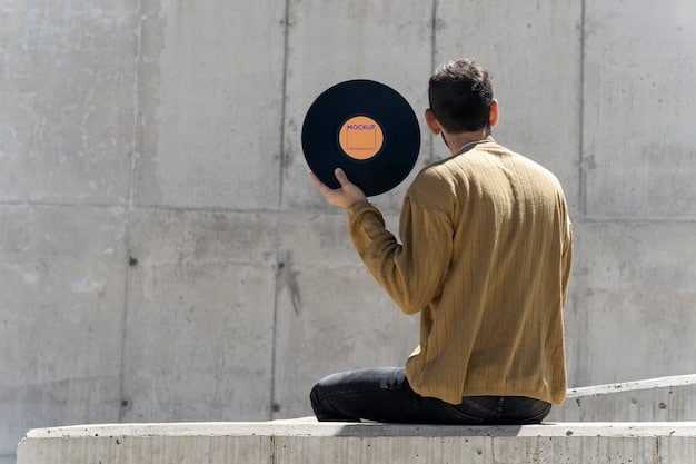 A high-angle shot of a person holding a vinyl record, with the album cover prominently displayed. The record is positioned in front of a vintage record player, partially visible in the background. The individual has tattoos on their forearm, one reads IS, another says music.