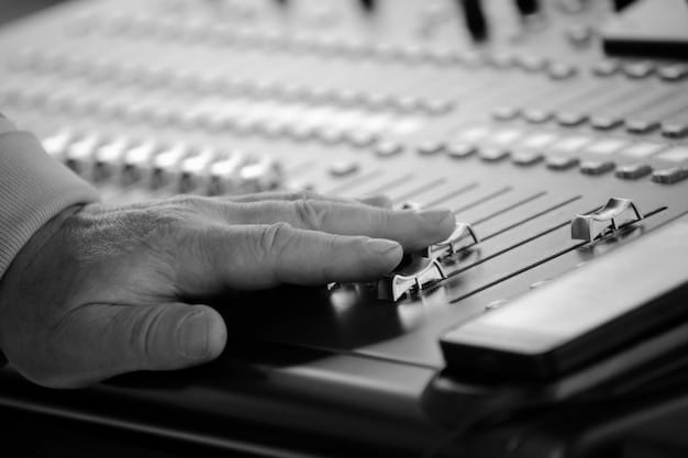 A black and white photograph of a vintage music studio console, focusing on the knobs and dials. The image conveys a sense of craftsmanship and the meticulous process of music production.