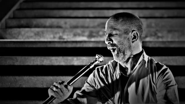 A black and white image of Maynard James Keenan singing intensely into a microphone during a Tool concert, conveying the passion and emotion he puts into his vocal performances.