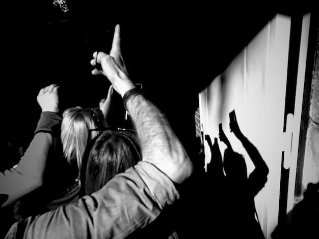 A black and white photo of concert attendees with hands raised in the air. The focus is on the crowd's energy and connection to the music, with blurred figures and stage lights creating a sense of movement and excitement.