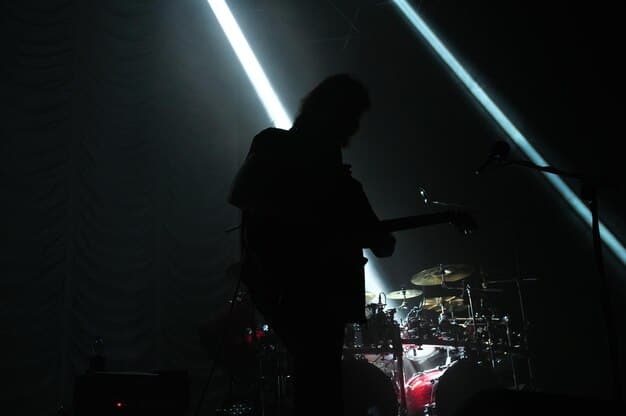 A dimly lit stage where a drummer's silhouette can be seen during a metalcore performance, capturing the energy and raw emotion of the song. The scene is filled with dark shadows and the drummer is striking the symbols with full force.