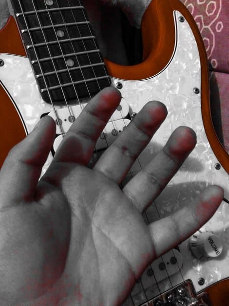 A close-up shot of a guitarist's hands playing a heavily distorted guitar with various effects pedals visible, emphasizing the importance of texture and sound manipulation in post-metal.