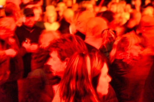 A close-up shot of a fan's face in the crowd at a heavy metal concert, illuminated by stage lights. The fan is singing along passionately, with a look of intense enjoyment on their face.