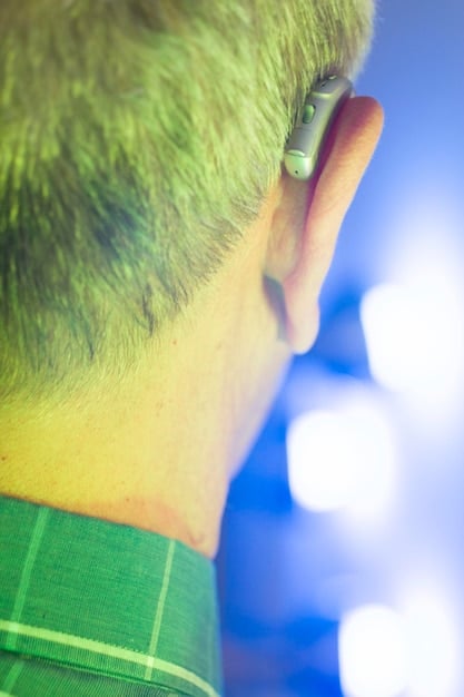 A close-up of a pair of earplugs, clearly showing the attenuation level in decibels. The background is blurred, showing a concert venue.