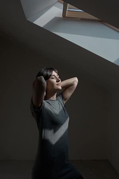 A person gently stretching their neck muscles, with a serene expression, in a dimly lit room with soft lighting.