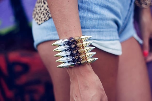 A person wearing a variety of heavy metal accessories: a spiked wristband, a chunky silver necklace with a skull pendant, and several rings with gothic designs; the background is dark and blurred, focusing attention on the accessories.