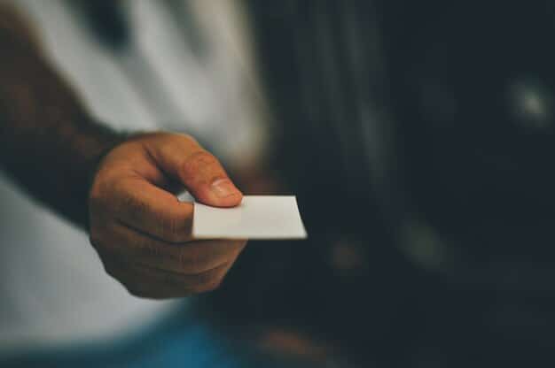 A close-up photo of a hand holding a diverse set of identification cards (driver's license, student ID, tribal ID) over a blurred background of a polling station.