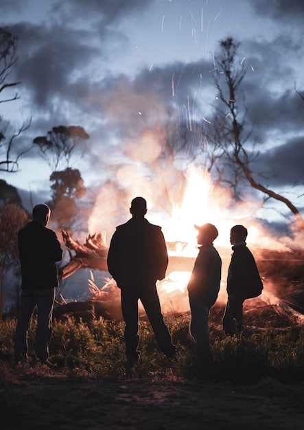 A medium shot facing forward, focusing on a group of armed soldiers walking through a dense forest under a cloudy sky. The light is diffused, creating a sense of tension and uncertainty.