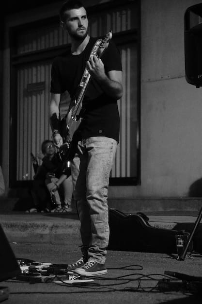 A candid, slightly blurred, black and white photo of a rock musician sitting alone backstage, head in hands, looking exhausted and overwhelmed. The background is dimly lit and shows glimpses of road cases and equipment.